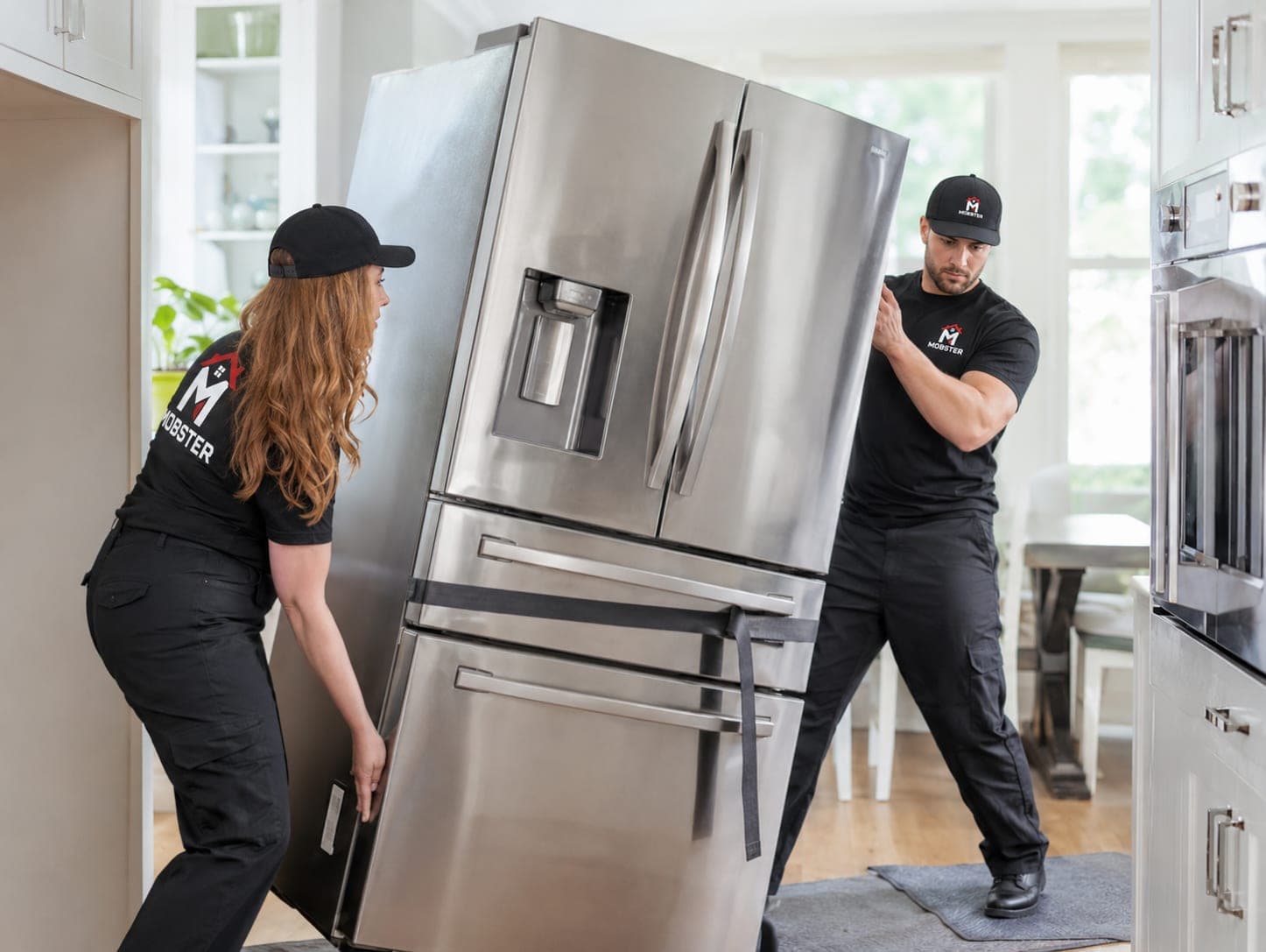 Two Mobsters walking a stainless steel refrigerator into a kitchen