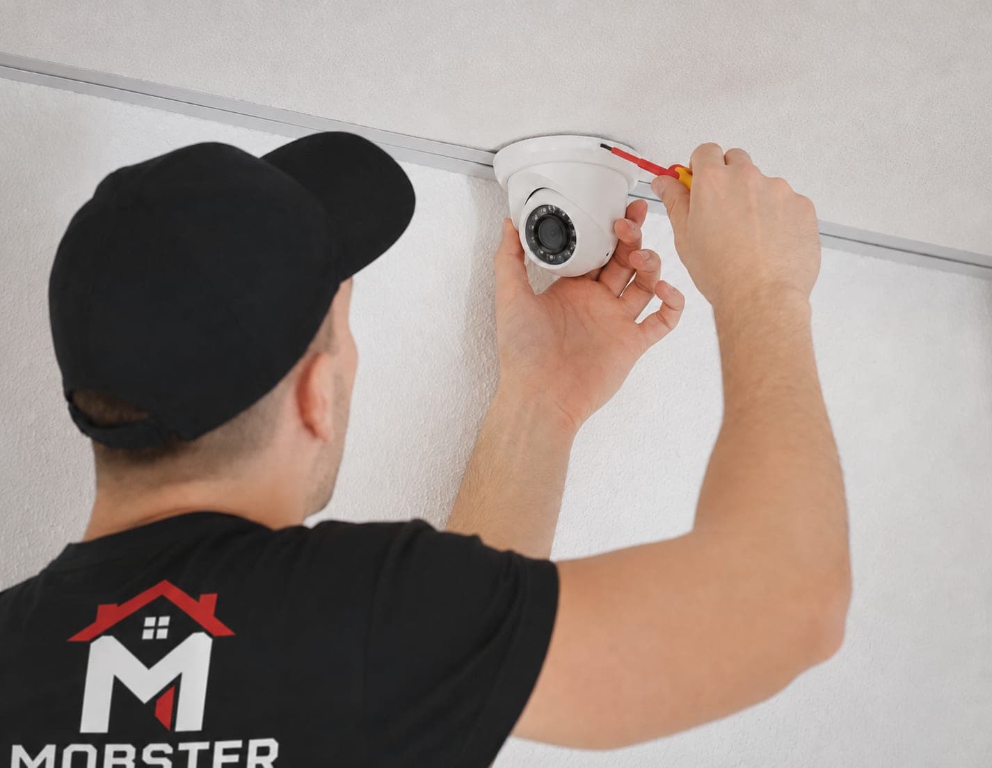 A Mobster mounting a dome security camera to a ceiling