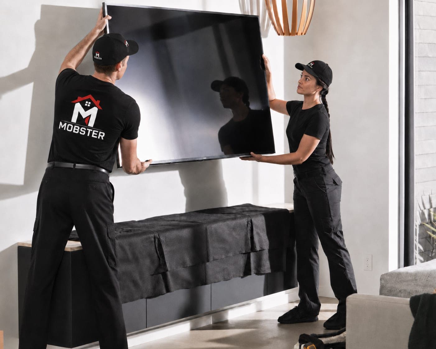 Two Mobsters lifting a large flat-screen television onto a living room wall